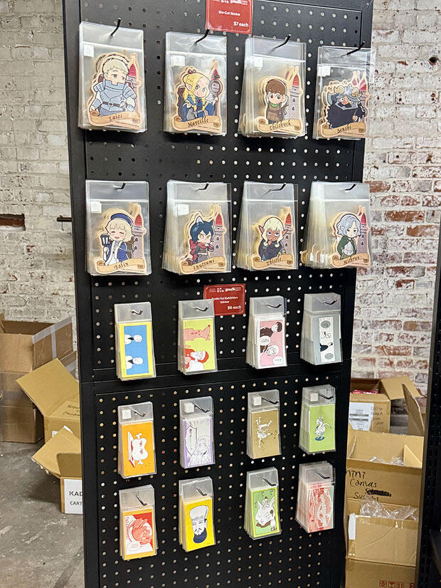 物販コーナー、『ダンジョン飯』と「九井諒子展」のオリジナルステッカー。他に、アクリルスタンド、缶バッジ、Tシャツ、複製原画なども販売中。